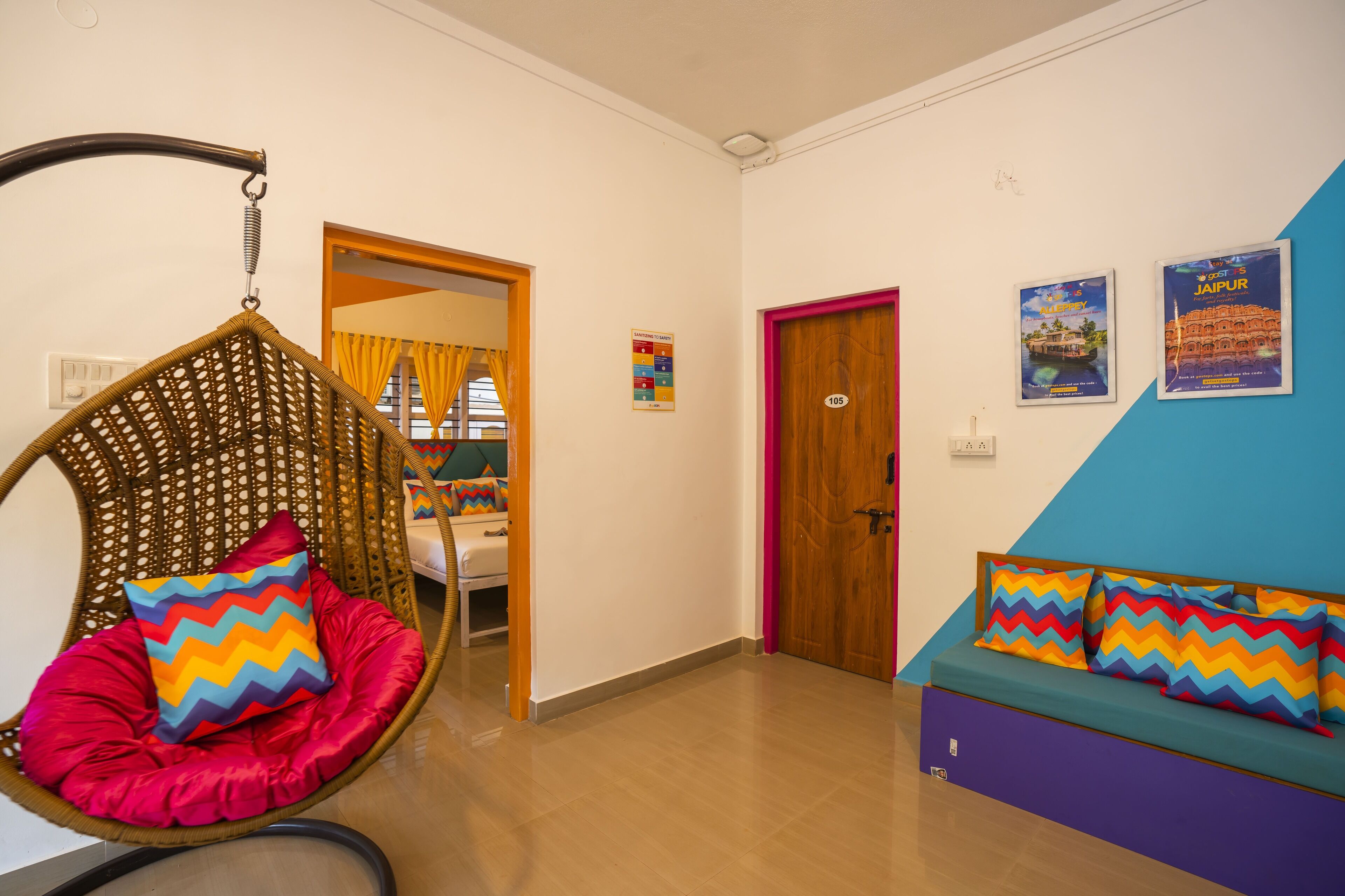 Una habitación con una silla colgante, un sofá, una puerta y dos carteles en la pared.