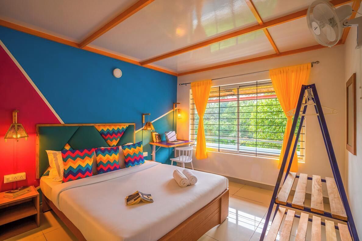 A bedroom with a bed, a desk, a chair, a ladder, and a window with curtains.