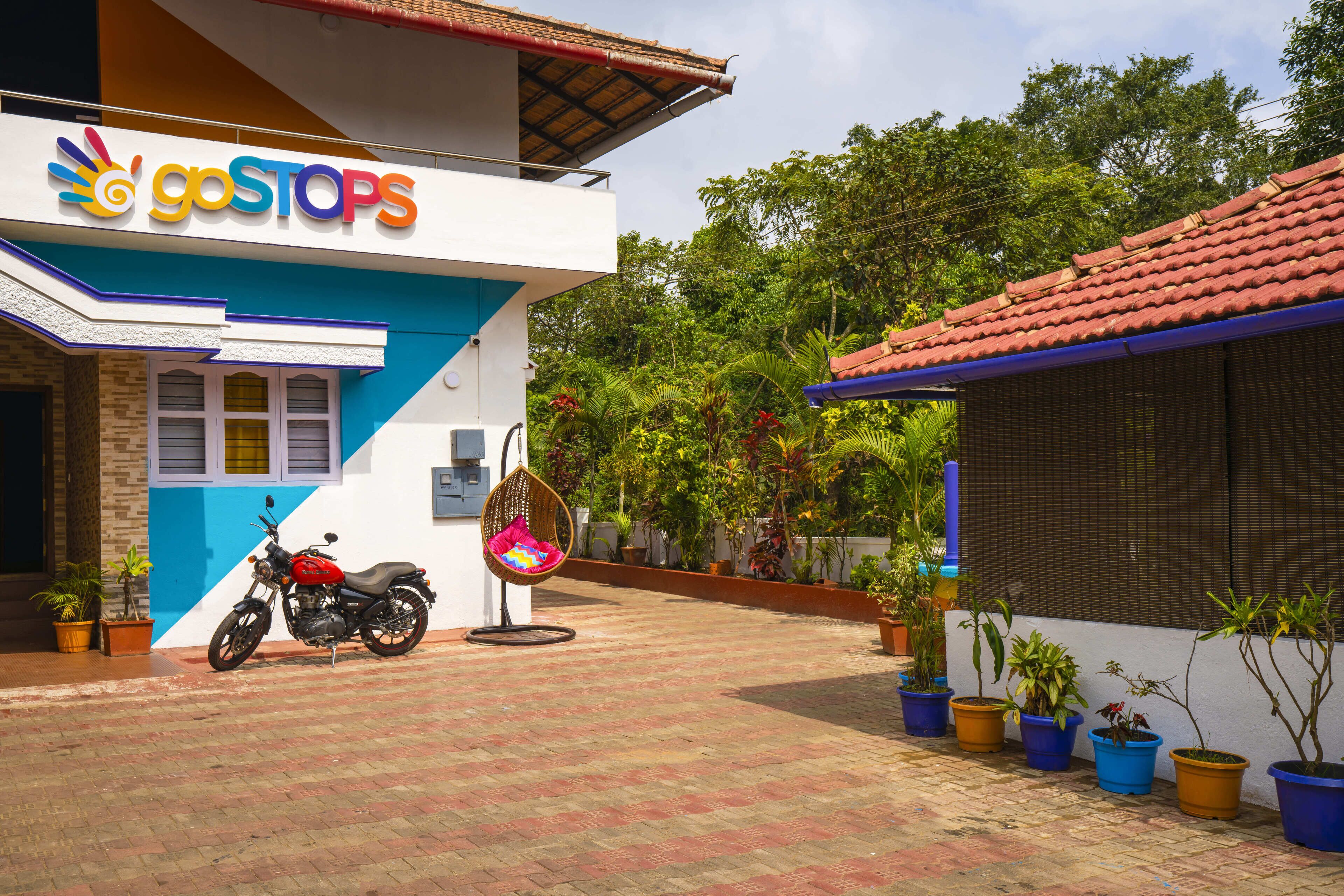 A building with a 'goSTOPS' sign, a motorcycle parked outside, and potted plants along the pathway.