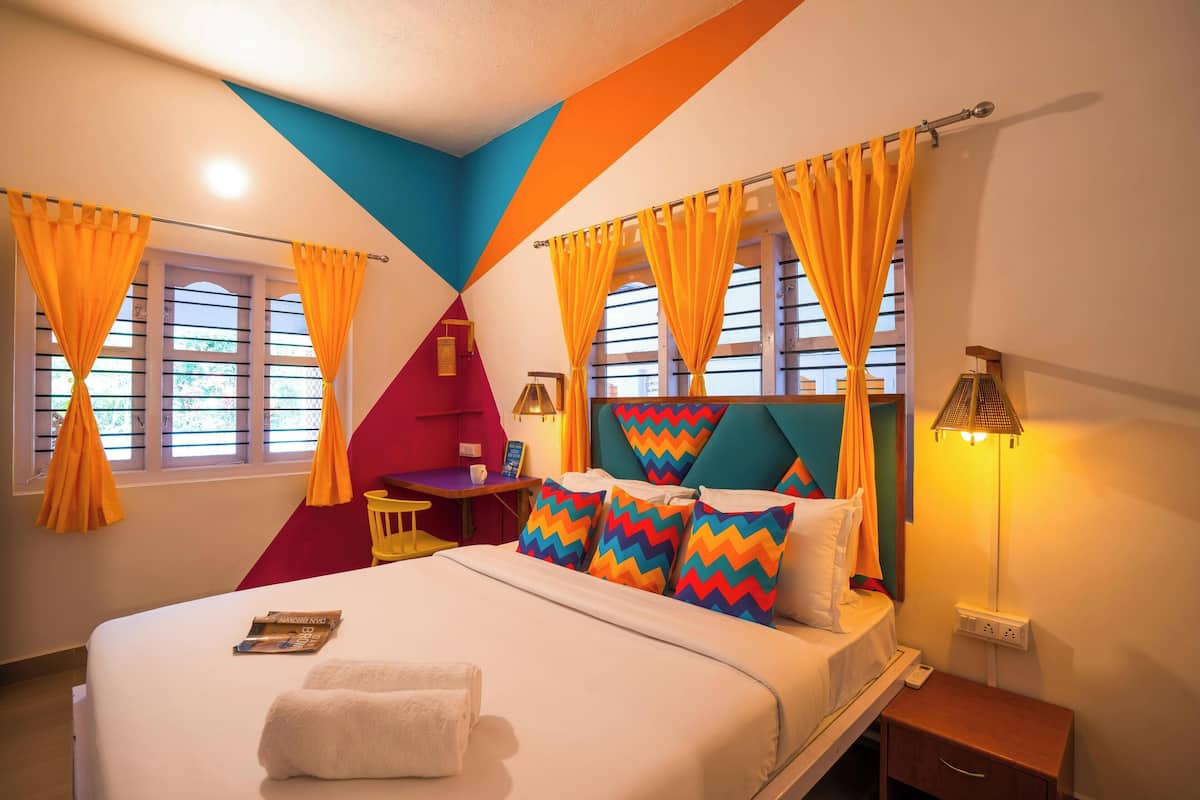 A hotel room with a bed, curtains, a nightstand, a lamp, and a window with shutters.