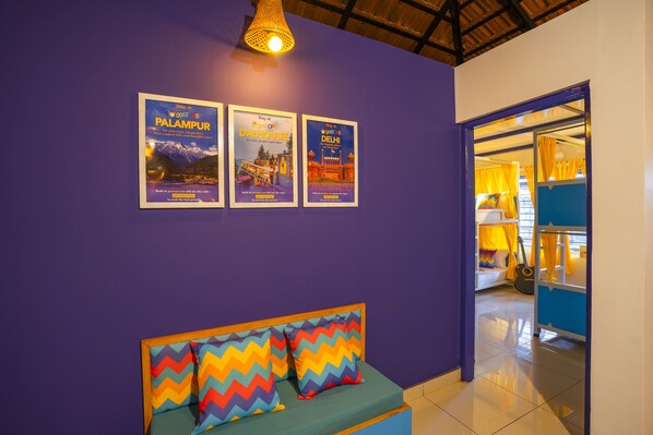 A room with a purple wall, a bed with colorful zigzag pillows, and three framed posters advertising travel destinations. - goSTOPS Coorg (Madikeri)