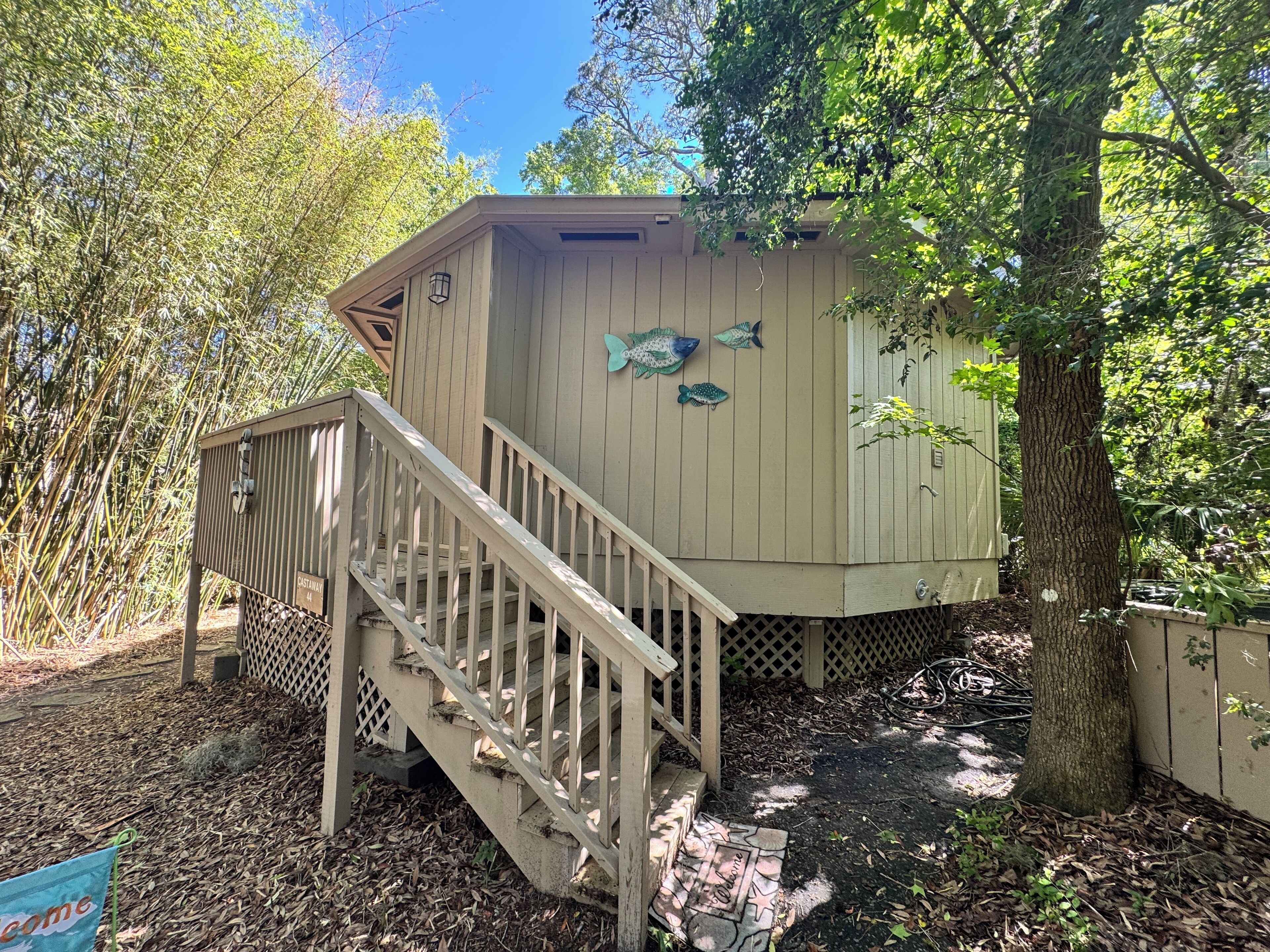 Una cabana de fusta amb una escala que condueix a una terrassa, envoltada d'arbres i un rètol que diu 'Welcome'.