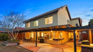 Ein zweigeschossiges Haus mit überdachter Terrasse, Grill und Sitzgelegenheit.