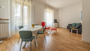 Un salon spacieux doté d’un plancher en bois, d’une table de salle à manger ronde avec des chaises, d’un canapé et d’une petite table d’appoint agrémentée d’une plante.