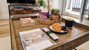 A wooden coffee table with a magazine, a remote control, a croissant, a cup of coffee, and a decorative pineapple centerpiece. - Bright 1-Bed Flat Near Fulham Broadway Station (London)