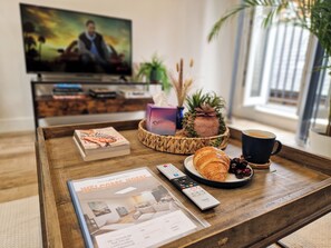 A wooden coffee table with a magazine, a remote control, a croissant, a cup of coffee, and a decorative pineapple centerpiece.
