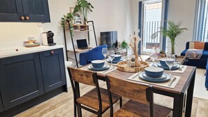 A modern kitchen with dark cabinets, a dining table set for four, and a living area with a sofa and a TV. - Bright 1-Bed Flat Near Fulham Broadway Station (London)