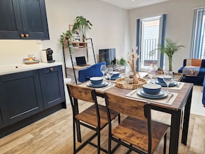 A modern kitchen with dark cabinets, a dining table set for four, and a living area with a sofa and a TV.