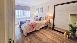 A bedroom with a bed, bedside lamps, a window with blinds, and a mirror. - Bright 1-Bed Flat Near Fulham Broadway Station (London)