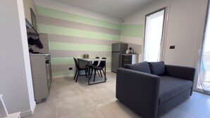A modern kitchen with a dining area, a sofa, and a large window.