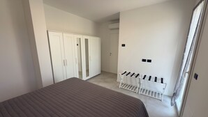 A bedroom with a bed, a wardrobe, a drying rack, and a door leading to another room.
