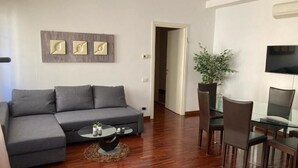 A modern living room with a grey sectional sofa, a round coffee table, and a dining area with a glass table and chairs. - Accomodo MIT51 Trivano Cenisio  (Milan)