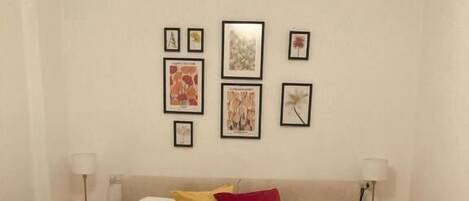 A neatly made bed with white linens and two pillows, a bedside table with a lamp, and a wall with framed pictures.