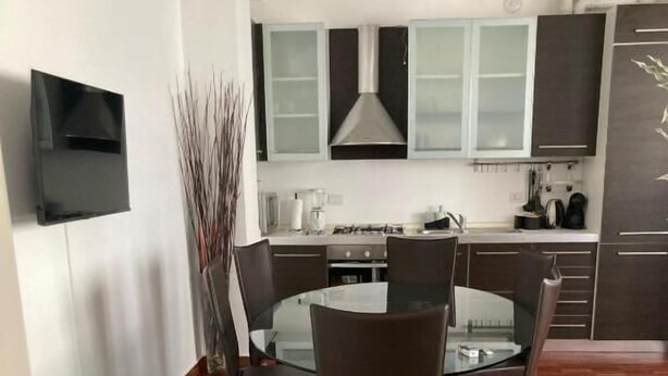 A modern kitchen with dark cabinets, a central island, and a flat-screen TV mounted on the wall. - Accomodo MIT51 Trivano Cenisio  (Milan)