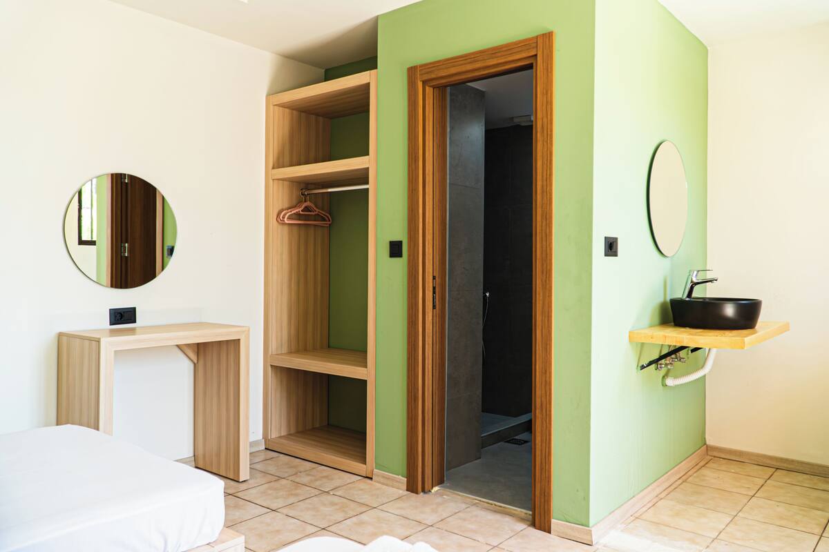A room with a bed, a wooden desk, a wardrobe, a mirror, and a sink.