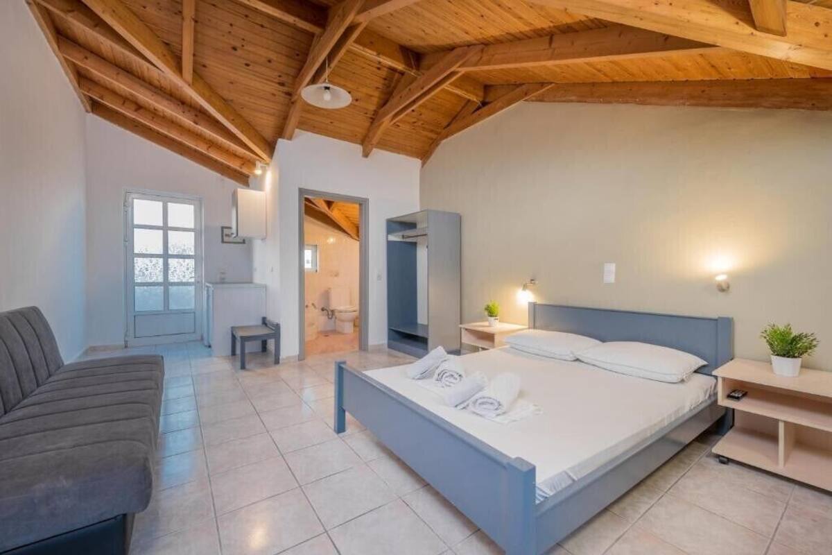 A bedroom with a bed, a sofa, a bedside table, and a window.