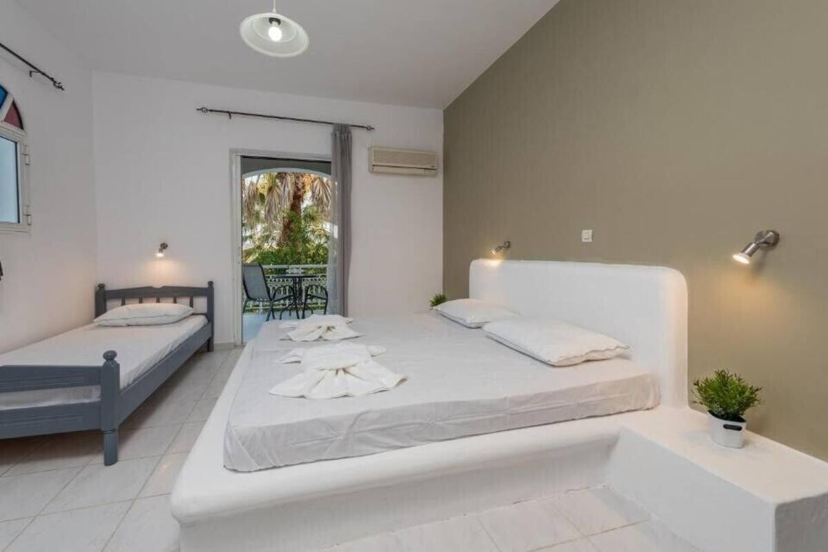 A bedroom with two single beds, a large bed, a small table, a potted plant, and a balcony with a view of greenery.