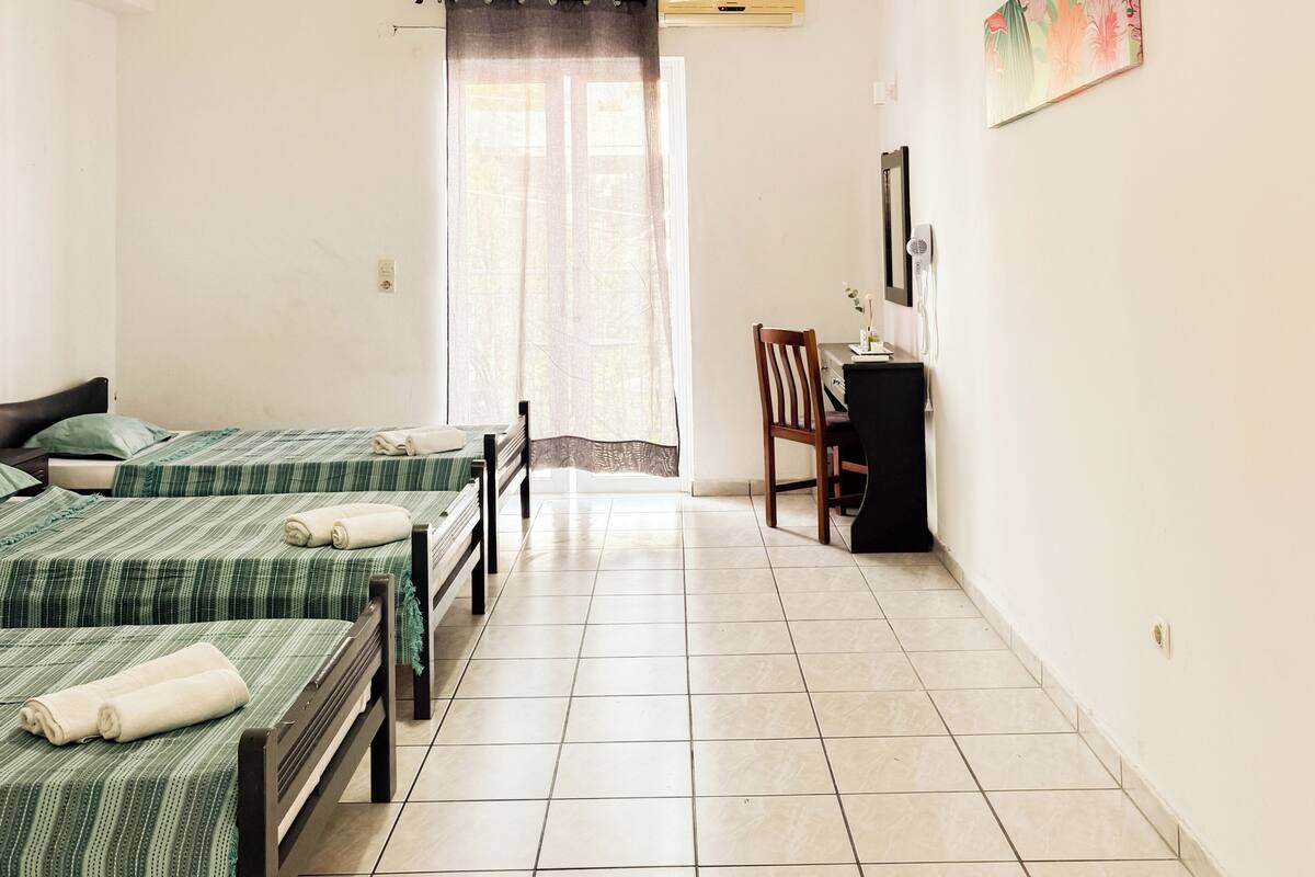 A room with two beds, a desk, a chair, a hanging light, and a window with curtains.