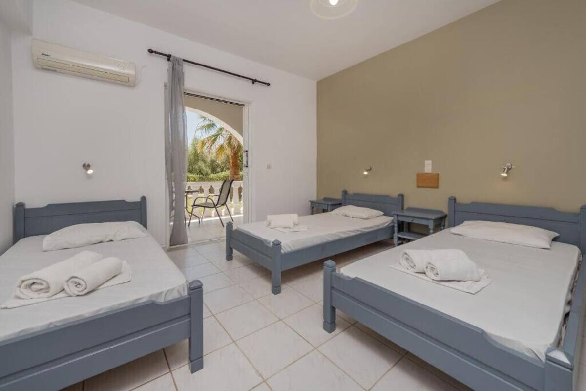 A hotel room with three single beds, a balcony with a view, and an air conditioning unit.