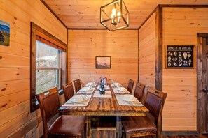 Comedor de madera con una mesa dispuesta para seis personas, una araña y un letrero que enumera animales del bosque.