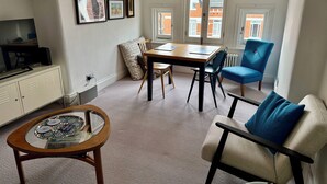 A living room with a dining table, chairs, a sofa, a TV, and framed pictures on the wall.