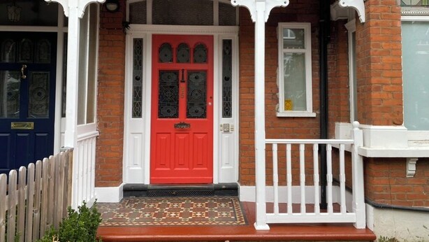 A red door with a white porch and a small white railing.
