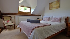 A bedroom with a large bed, a chair, a nightstand, a window, and a painting on the wall. - Cosy 18th century cottage. Pet friendly. Absolute tranquility! (Mitcheldean)