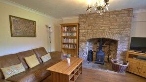 A cozy living room with a stone fireplace, a wooden bookshelf, a leather sofa, and a television on a wooden stand. - Cosy 18th century cottage. Pet friendly. Absolute tranquility! (Mitcheldean)