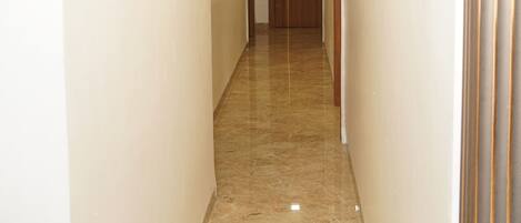 A hallway with a marble floor, white walls, and a wooden door at the end.
