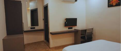 Een hotelkamer met een bed, een bureau, een televisie, een spiegel en een airconditioner.