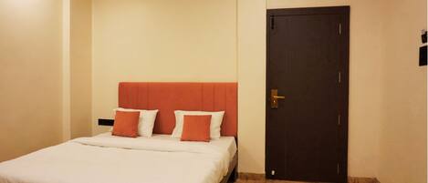 A hotel room with a bed, a dark door, and a light-colored wall.