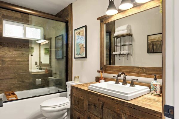 A bathroom with a glass shower enclosure, a white toilet, a wooden vanity with a sink, and a large mirror. - EV-Charged Treetop Cabin w/ Game Room & Decks (Lake Arrowhead)