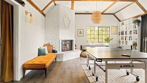 A room with a ping pong table, a fireplace, a bookshelf, and a window with natural light.