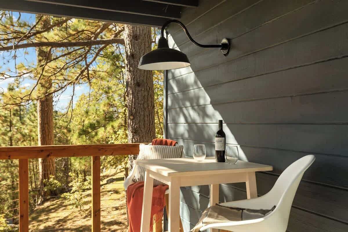 En träveranda med ett bord och stolar, en flaska vin och en lampa.