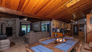 A spacious living area with a wooden ceiling, a stone fireplace, and a large dining table with blue placemats. - Newly Listed! Lakefront Home Private Dock with Huge Views (Camdenton)