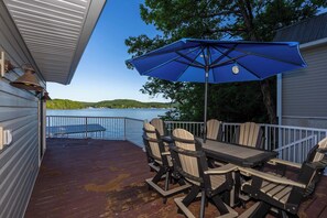 A deck with outdoor furniture, a blue umbrella, and a view of a lake. - Newly Listed! Lakefront Home Private Dock with Huge Views (Camdenton)