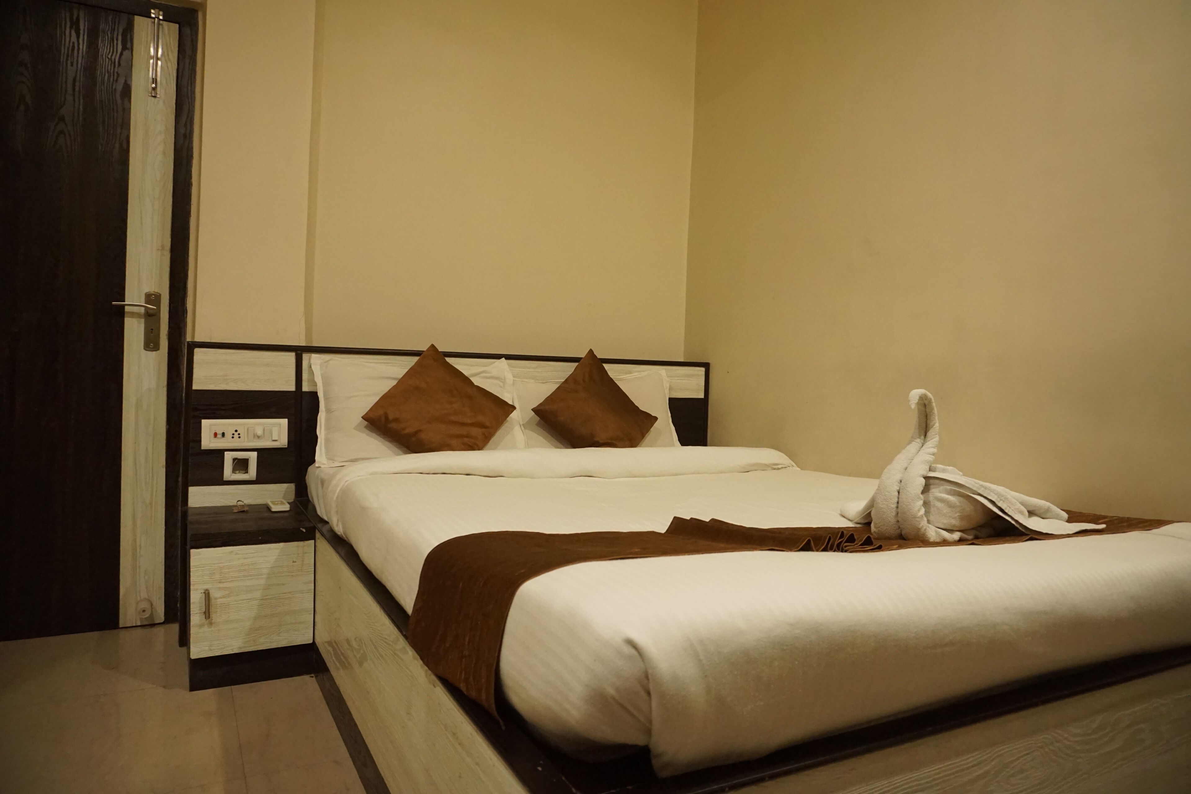 A neatly made bed with a brown blanket and pillows, a bedside table with a phone, and a door to the left.