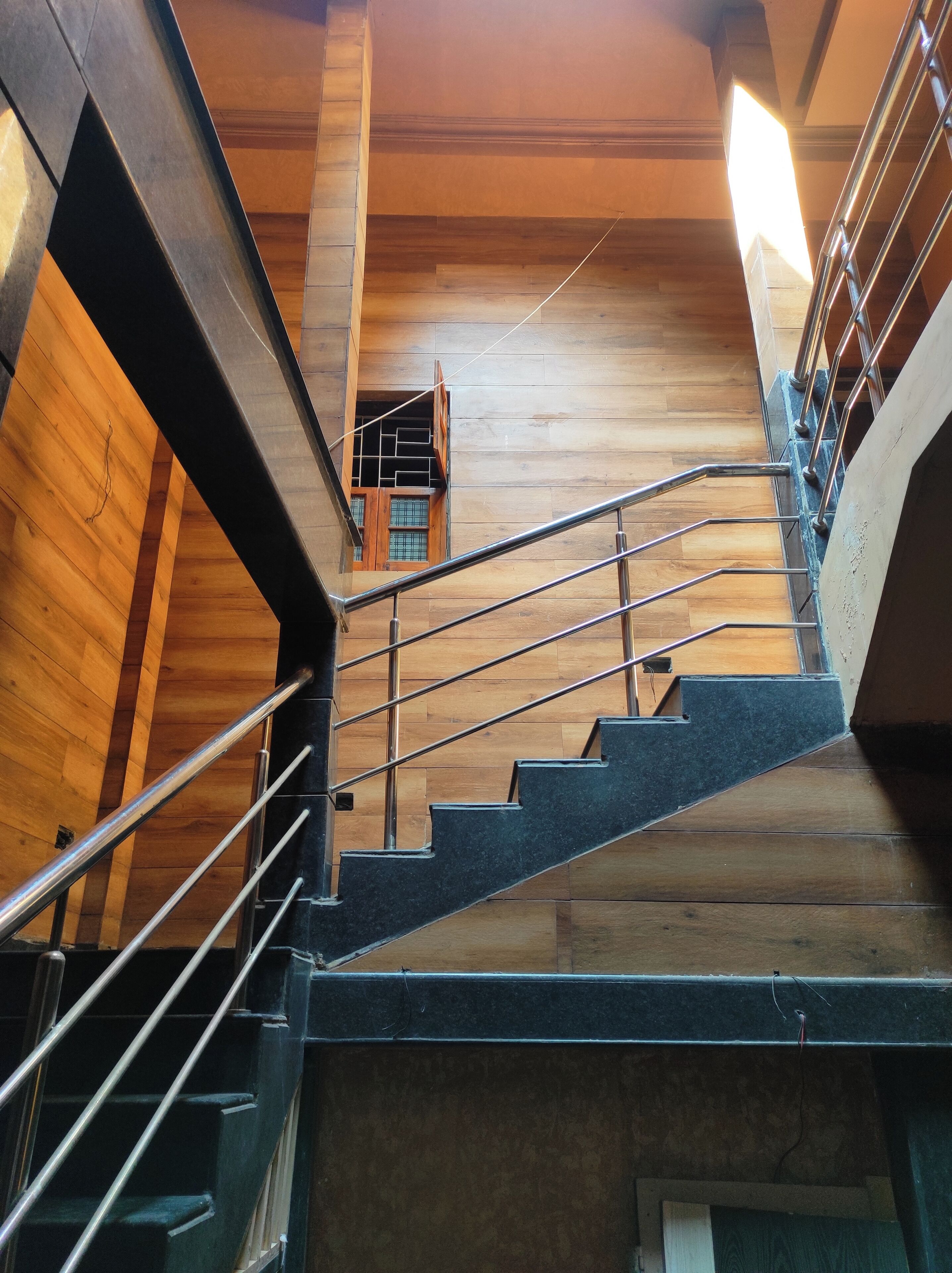 A staircase with metal railings and wooden steps, leading to an upper floor with a view of a wooden interior.