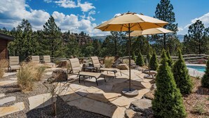 Une terrasse extérieure avec un sol en pierre, plusieurs fauteuils de jardin, une table et un grand parasol.