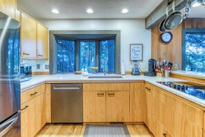 A modern kitchen with wooden cabinets, a dishwasher, a stove, and a window with a view of trees.