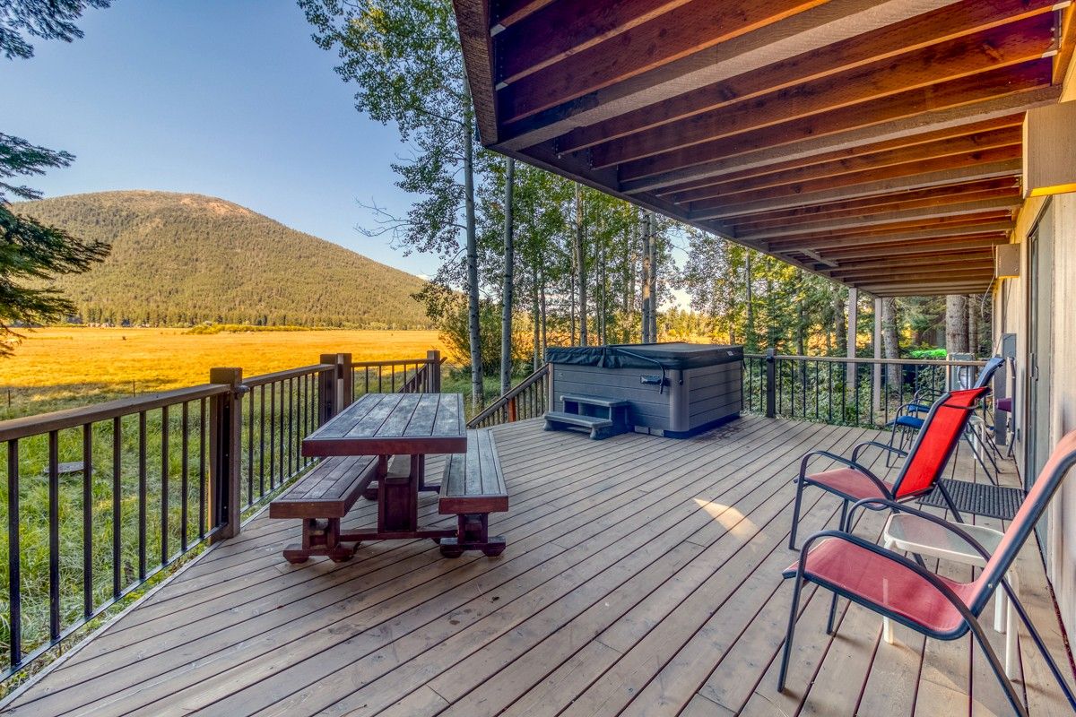 Une terrasse en bois avec une table de pique-nique et des chaises, un jacuzzi et une vue sur une colline boisée.