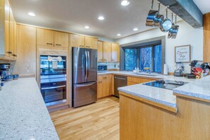 Cozinha moderna com armários de madeira, eletrodomésticos de aço inoxidável e uma janela grande que proporciona iluminação natural.