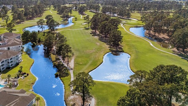 A golf course with multiple ponds and a large building with a swimming pool. - Myrtlewood Unit 103 - Golf Area! (Myrtle Beach)