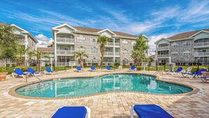 A swimming pool with lounge chairs, a brick deck, and a multi-story building with balconies in the background. - Myrtlewood Unit 103 - Golf Area! (Myrtle Beach)