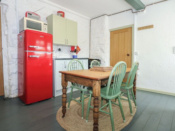 A compact kitchen with a red refrigerator, a wooden dining table, and green chairs.
