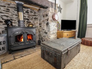 Una chimenea de piedra con un horno negro, un cofre de madera y un televisor sobre un mueble de madera.