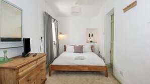 A bedroom with a wooden bed, a dresser, a mirror, and a bedside lamp. - Cobweb Cottage (Caernarfon)