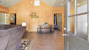 A room with a wooden wall, a dining table, and a sofa. There are signs indicating room numbers and names.