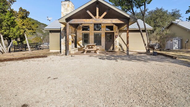 A rustic building with a stone chimney, wooden beams, and a picnic table in front.