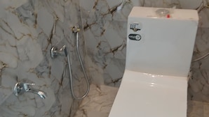A bathroom with a toilet, a shower, and a marble wall. - Awadh Biharee Inn (Faizabad)